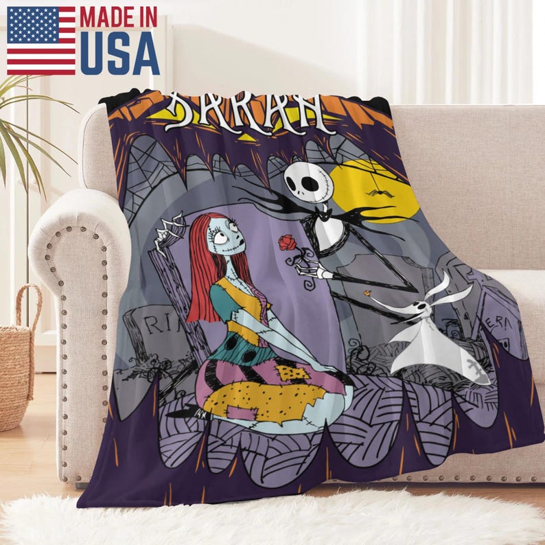 May include: A plush throw blanket featuring a scene from The Nightmare Before Christmas. The design includes Jack Skellington offering a rose to Sally, with Zero nearby. The blanket has a purple border and the word "SARAH" is at the top.