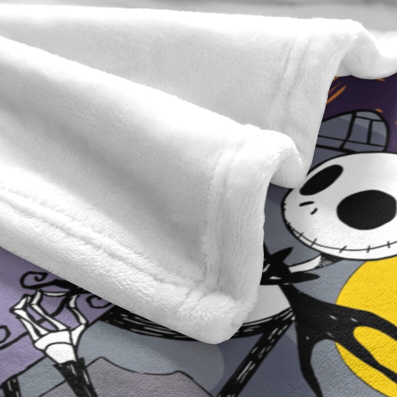 May include: White plush blanket with a corner featuring a cartoon character with a skull face, wearing a black suit and a bat-shaped bow tie. The background includes a yellow moon and a purple sky.