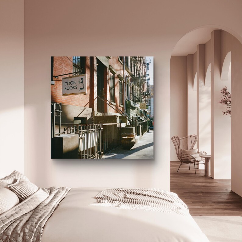 May include: A framed print of a New York City street scene. The image features a brick building with a sign that reads "COOK BOOKS." The scene includes a wrought iron fence, steps, and fire escapes.
