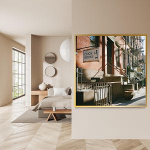 May include: A framed photograph of a New York City street scene. The image features a brick building with a sign that reads "COOK BOOKS". The sign has a silhouette of a chef. The photograph is displayed in a gold frame.