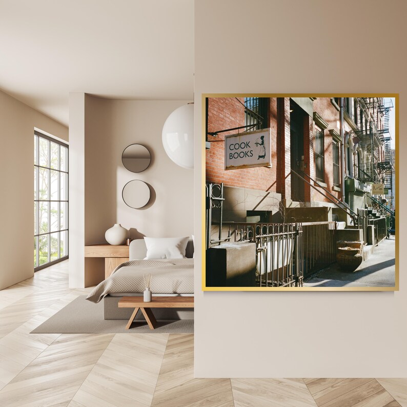 May include: A framed photograph of a New York City street scene. The image features a brick building with a sign that reads "COOK BOOKS". The sign has a silhouette of a chef. The photograph is displayed in a gold frame.