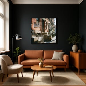 May include: A living room with a burnt orange sofa, a round wooden coffee table, and a beige armchair. A framed picture of a street scene hangs on the dark wall. A floor lamp and a wooden cabinet complete the decor.