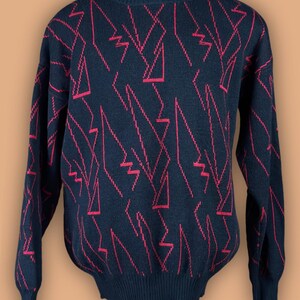 May include: Black sweater with a red geometric pattern. The long-sleeved sweater has a crew neck and ribbed cuffs and hem. The red pattern consists of zigzags and angular lines, creating a bold, graphic design. The sweater is displayed on a mannequin.