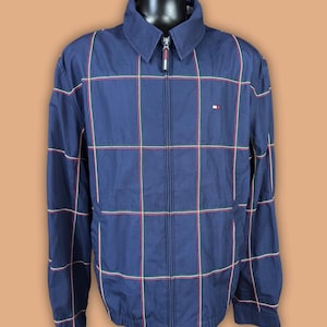 May include: A navy blue zip-up jacket with a plaid pattern in red, white, and green. The jacket has a collared neckline and a small logo on the chest. The jacket is displayed on a mannequin.