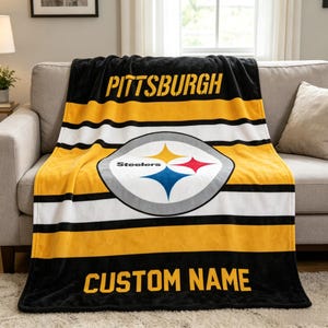 May include: A black, yellow, and white fleece throw blanket featuring the Pittsburgh Steelers logo in the center. The word PITTSBURGH is printed in yellow at the top, and the text CUSTOM NAME is printed in yellow at the bottom of the blanket.