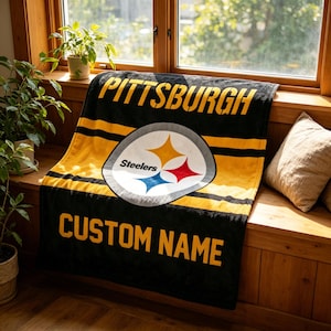 May include: A black and yellow fleece blanket featuring the Pittsburgh Steelers logo in the center, the word PITTSBURGH at the top, and the text CUSTOM NAME at the bottom. The design includes horizontal yellow stripes across the black fabric.