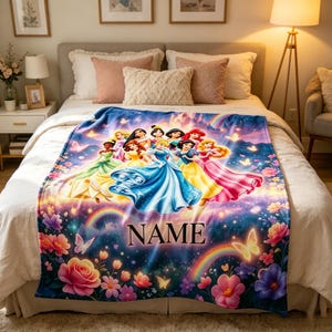 May include: A plush, colorful blanket featuring a group of animated princesses in their gowns. The blanket has a blue background with flowers, butterflies, and rainbows. The word "NAME" is printed in large letters.