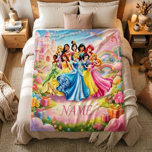 May include: A soft fleece blanket featuring a colourful illustration of multiple animated princesses standing in front of a castle, rainbow, and candy-themed landscape, with the word NAME printed in pink script at the bottom centre.