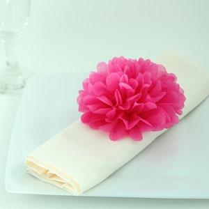 Puede incluir: Una servilleta blanca con una flor de papel rosa en la parte superior, colocada en un plato blanco.