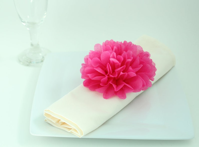 Puede incluir: Una servilleta blanca con una flor de papel rosa en la parte superior, colocada en un plato blanco.