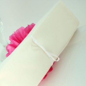 Puede incluir: Una servilleta blanca atada con una cinta blanca alrededor de un pomp&oacute;n de papel de seda rosa.