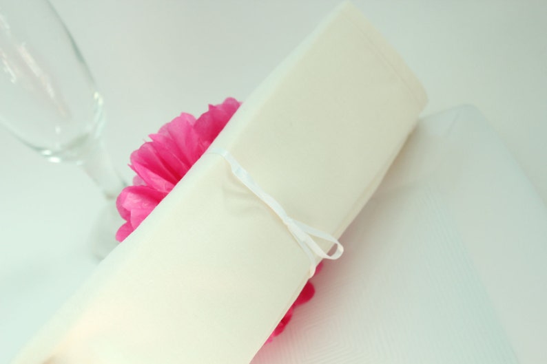 Puede incluir: Una servilleta blanca atada con una cinta blanca alrededor de un pomp&oacute;n de papel de seda rosa.