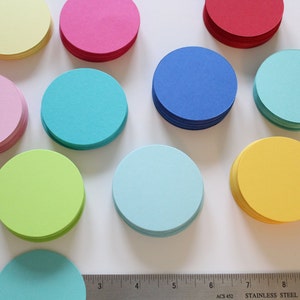 May include: A collection of ten stacks of colorful paper circles. The circles are in the following colors: yellow, pink, blue, turquoise, green, light blue, and orange.