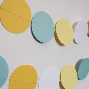 May include: A garland of paper circles in yellow, white, and light blue. The circles are strung together with white thread.