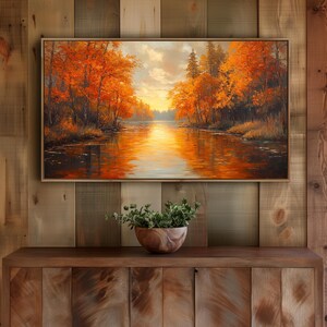 Könnte beinhalten: Gerahmtes Landschaftsgemälde, das eine Flussszene bei Sonnenuntergang zeigt. Das Kunstwerk zeigt leuchtend orange und rote Herbstbäume, die die Ufer säumen und sich im Wasser spiegeln. Der Himmel ist eine Mischung aus goldenen und wolkigen Farbtönen.