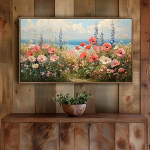 May include: A rectangular framed oil painting depicting a coastal meadow filled with vibrant red, pink, and white poppies alongside tall blue wildflowers, set against a backdrop of a calm blue sea and a sky with soft white clouds.