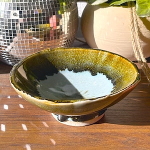 May include: A white ceramic mug with a black handle and the text "But first, coffee" in a handwritten style. The mug is on a white surface. The mug is approximately 4 inches tall.