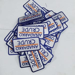 Puede incluir: Un montón de parches rectangulares con fondo blanco y bordes azules. Los parches tienen las palabras "CRUDE" y "ANADARKO" bordadas en azul y naranja.