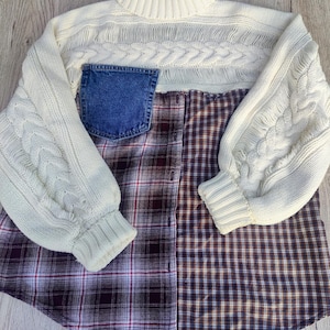 Könnte beinhalten: Ein cremefarbener Pullover mit Zopfmuster an den Ärmeln und am oberen Brustbereich. Er hat eine Jeans-Tasche und ein Flanellhemd im Design. Der Pullover hat einen Rollkragen.