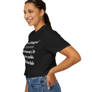 A woman wearing a black t-shirt with white text and a ponytail is smiling and looking to the side.