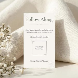 Puede incluir: Una tarjeta blanca con el texto "Follow Along" y detalles sobre actualizaciones de redes sociales. Incluye un espacio para un código QR e información de la tienda, sobre un fondo de tela blanca suave con delicadas flores blancas.