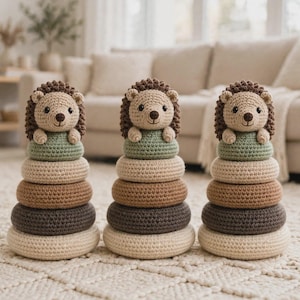 May include: Three crochet stacking toys, each featuring a beige hedgehog topper with dark brown spines. Below each hedgehog are four stacked rings in shades of sage green, cream, tan, and dark brown, arranged in a vertical column on a flat surface.