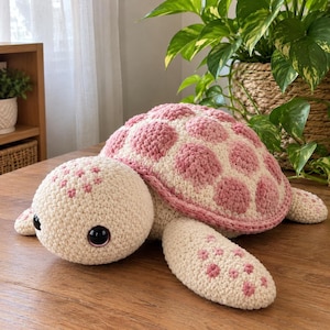Può includere: Un peluche a forma di tartaruga realizzato all'uncinetto, con corpo e testa color crema e grandi occhi in plastica nera. Il guscio presenta un motivo a macchie circolari alternate color crema e rosa tenue. Le pinne hanno piccoli dettagli ricamati in rosa.