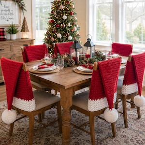 May include: A set of red and white crocheted Santa hat chair covers draped over wooden dining chairs. Each cover features a vibrant red body, a thick white brim, and a white pom-pom at the tip, creating a festive holiday look for the dining room.