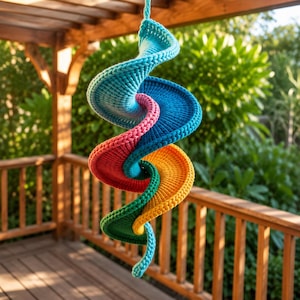 Puede incluir: Una colorida escultura colgante en forma de espiral. La obra está hecha de material de punto en tonos de azul, rosa, rojo, amarillo y verde. Se suspende de un cordón turquesa, creando una exhibición vibrante y llamativa.
