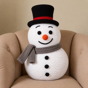 May include: A white crocheted snowman plush toy featuring a black top hat with a red band, a bright orange carrot-shaped nose, black embroidered eyes and mouth, three black buttons on the torso, and a textured grey knit scarf wrapped around its neck.