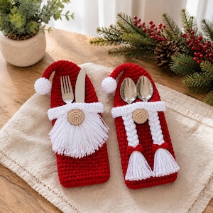 May include: Two red crochet cutlery holders shaped like gnomes with white pom-poms at the tips. One holder features a white yarn beard and a tan nose, holding a silver fork and knife. The other features white braided yarn pigtails and a tan nose.