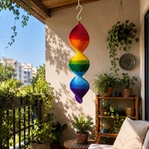 May include: A hanging spiral wind spinner crafted from crocheted yarn in a vibrant rainbow gradient. The structure features a continuous twisted shape transitioning from red at the top through orange, yellow, green, and blue to purple at the bottom.
