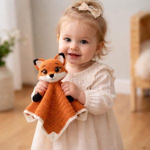 K&ouml;nnte beinhalten: Geh&auml;kelte Fuchs-Kuscheldecke in Orange, Wei&szlig; und Schwarz. Der Fuchs hat ein freundliches Gesicht und ist an einer quadratischen Decke befestigt. Ein weiches, handgefertigtes Produkt f&uuml;r Babys und Kleinkinder.