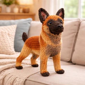 Pode incluir: Figura de cão de crochê artesanal em tons de castanho, bege e preto. O cão tem orelhas eretas, focinho escuro e cauda curta. Está posicionado em pé sobre uma superfície clara, mostrando o detalhado trabalho de crochê.