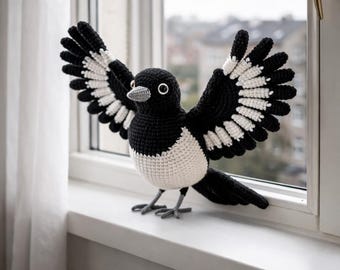May include: A crocheted magpie, predominantly black and white, with wings spread wide. The bird is positioned on a windowsill, with a detailed beak and eye. This handcrafted item is a decorative piece, suitable for home decor.