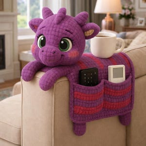 May include: A purple dragon-shaped couch arm organizer with two pockets and a cup holder. The dragon has large green eyes, pink cheeks, and a quilted texture. The pockets are striped with red and purple. A remote control and a small white device are in the pockets.