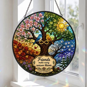 May include: A circular stained glass suncatcher featuring a tree representing four seasons, with a blue bird and a yellow bird perched on a branch. An infinity symbol sits between them. Text reads: Friends make every season bloom, ALWAYS & FOREVER.