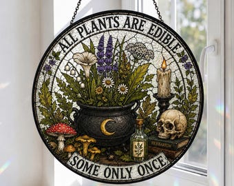 Puede incluir: Un atrapasueños circular de vidrieras que muestra un caldero negro con una luna creciente, rodeado de flores silvestres, setas, una vela encendida, una calavera y una botella pequeña. El texto dice ALL PLANTS ARE EDIBLE SOME ONLY ONCE.