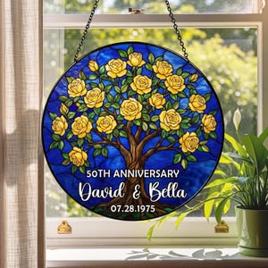 May include: Round stained glass window art with a blue background and a tree with yellow roses. The text reads "50th Anniversary" and the names "David & Bella" with the date "07.28.1975". The artwork is hanging in front of a window.