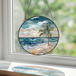 Puede incluir: Vidriera redonda que representa una escena de playa tropical con una palmera, olas del oc&eacute;ano y una orilla arenosa. La obra de arte presenta tonos de azul, verde y beige, con un marco de metal negro y una cadena para colgar.