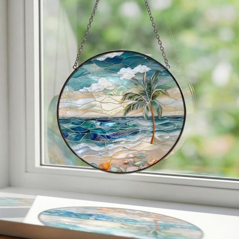 Puede incluir: Vidriera redonda que representa una escena de playa tropical con una palmera, olas del oc&eacute;ano y una orilla arenosa. La obra de arte presenta tonos de azul, verde y beige, con un marco de metal negro y una cadena para colgar.