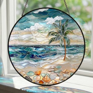 Puede incluir: Vidriera redonda que representa una escena de playa con una palmera, olas del oc&eacute;ano y conchas marinas. La obra de arte tiene un marco de metal negro y est&aacute; suspendida por una cadena. Los colores incluyen tonos de azul, verde, beige y blanco.