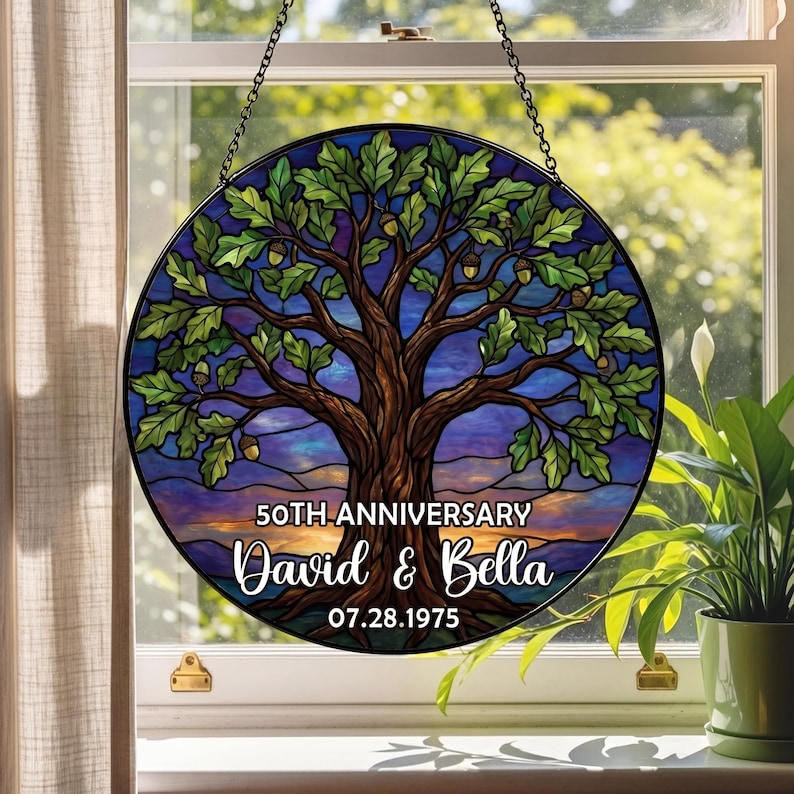 May include: Round stained glass window art featuring a tree with green leaves and acorns, set against a blue and purple background. The text reads "50th Anniversary" with the names "David & Bella" and the date "07.28.1975".