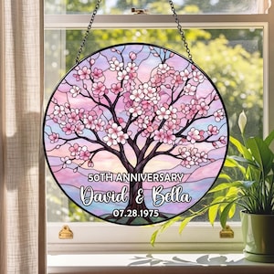 May include: Round stained glass window art with a cherry blossom tree design. The artwork features pink and white flowers, a brown tree trunk, and a pastel sky. Text reads "50th Anniversary" and "David & Bella 07.28.1975".