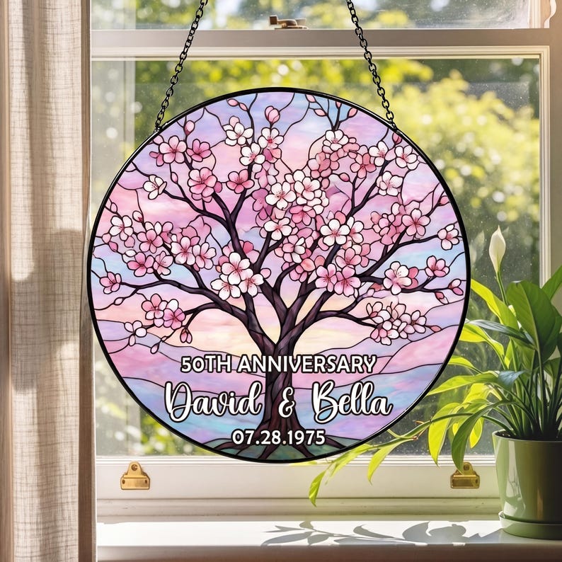 May include: Round stained glass window art with a cherry blossom tree design. The artwork features pink and white flowers, a brown tree trunk, and a pastel sky. Text reads "50th Anniversary" and "David & Bella 07.28.1975".