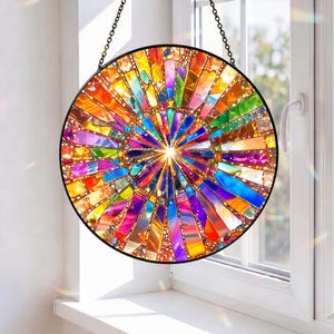 May include: A circular stained glass suncatcher featuring a vibrant radial pattern of multicolored glass segments in shades of red, orange, yellow, green, blue, and purple, held together by a black metal frame and suspended by a black chain.