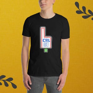 Puede incluir: Camiseta negra con un diseño de dedo de espuma blanco, ribete rojo y las letras "CRL" y el número "1" en azul y rojo. La camiseta la lleva una persona.