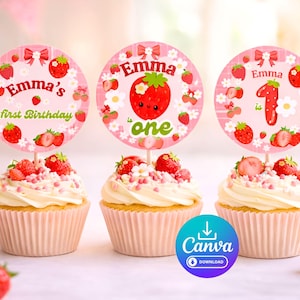 May include: Three cupcakes with pink liners and white frosting, topped with fresh strawberries and decorative toppers. The toppers are pink with strawberry and floral designs, and the name "Emma" is featured. The cupcakes are for a first birthday.