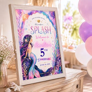 May include: A framed mermaid-themed birthday party sign. The sign reads "Let's make a SPLASH! Welcome to Amelia's 5th Birthday! June 18, 2026." The illustration features a mermaid with purple hair and a colorful tail, surrounded by aquatic plants.