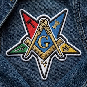 May include: Embroidered patch featuring a Masonic symbol with a compass, square, and the letter "G" at the center. The patch has a star shape with red, blue, green, and yellow accents. The patch is on a denim jacket.